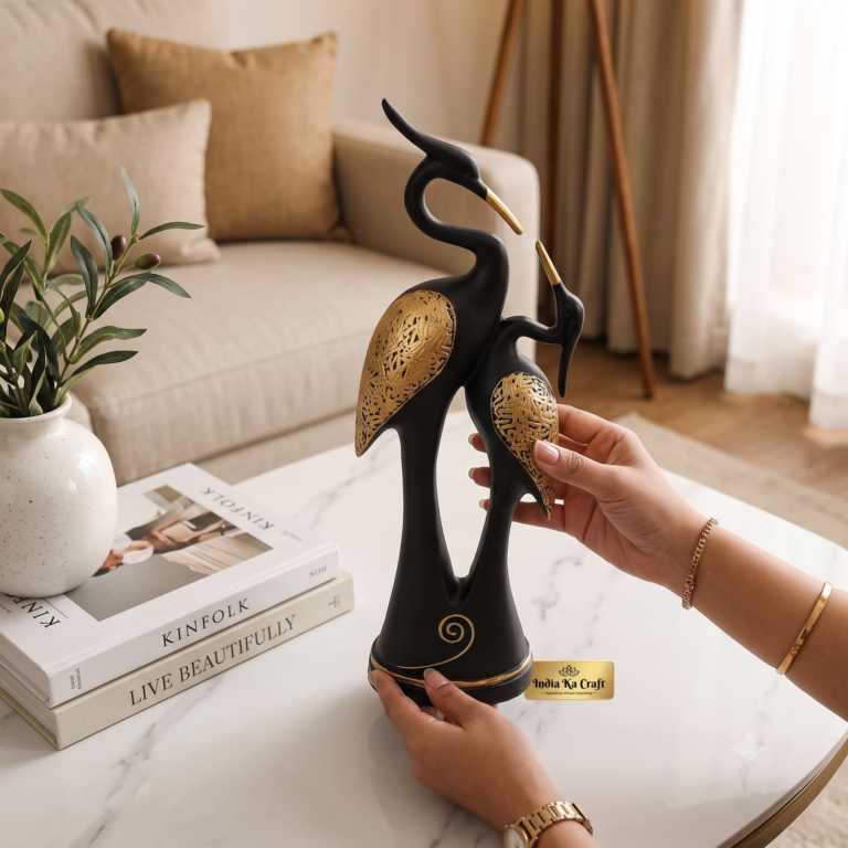 Top-angle hand-held view of Black Kissing Swan Couple Showpiece featuring matte black resin body with intricate golden carved wing detailing on a modern table setting by India Ka Craft.